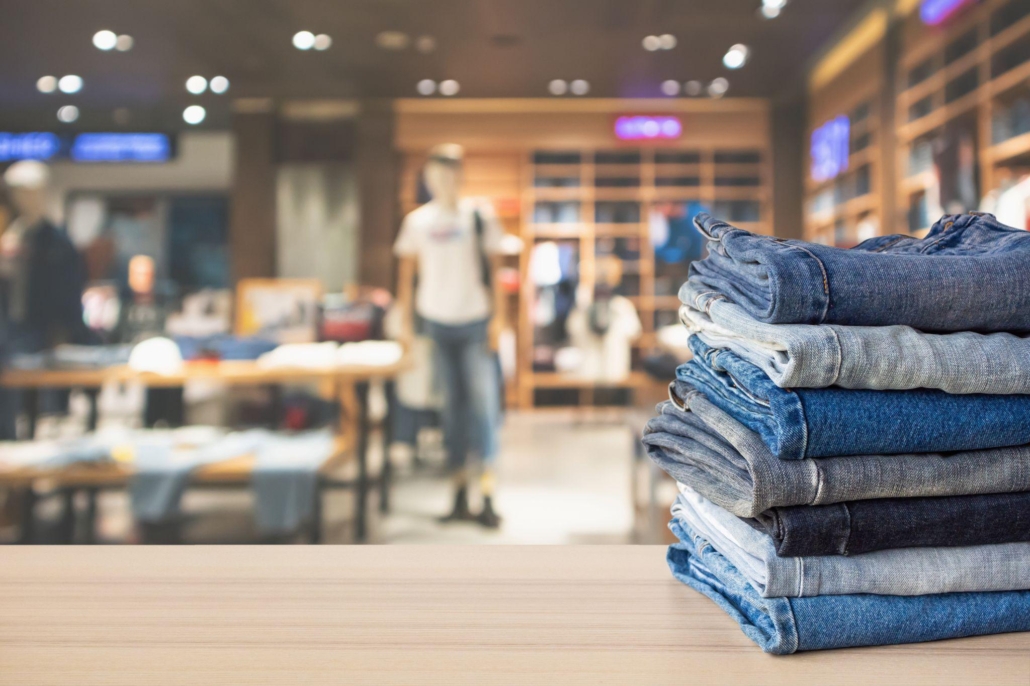 Blue denim jeans stack on wood table top with abstract blur clothing store in modern shopping mall